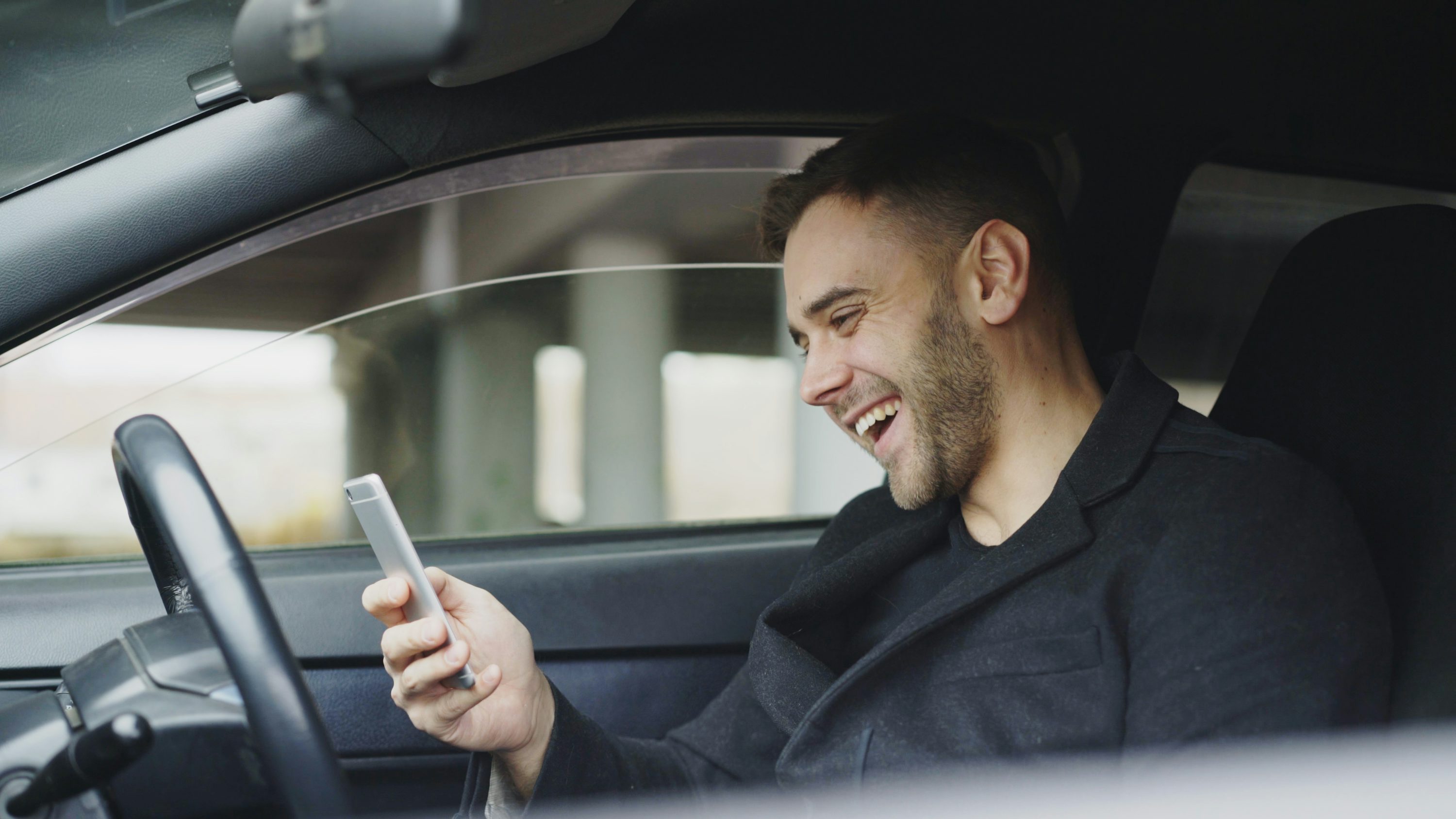 A smiling car owner sitting inside their modern vehicle, holding a smartphone and looking relieved
